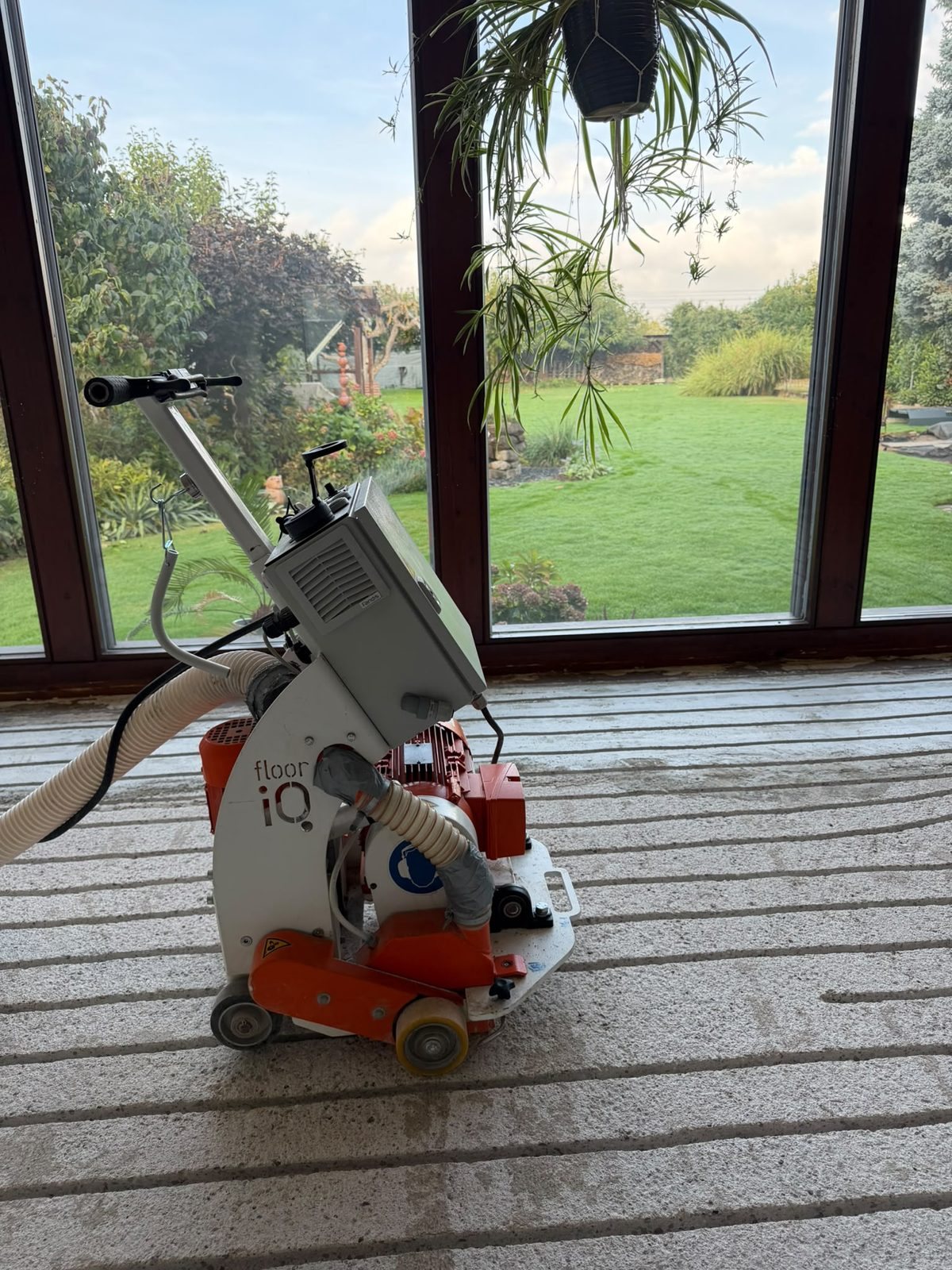 Bodenfräse mit angeschlossenem Absaugschlauch auf gefrästem Estrich im Wintergarten